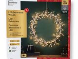 a white christmas wreath with led lights on a green background