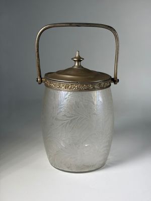 an antique glass ice bucket with a metal handle on a white surface