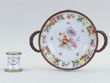 a white plate with a floral design on it next to a small cup