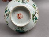a person holding a small white vase with green and red designs