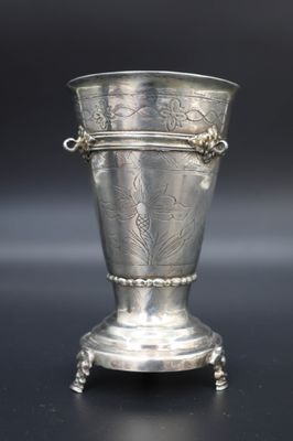 un vase ancien en argent posé sur un socle, sur une surface noire