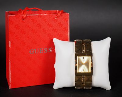 un oreiller blanc posé à côté d'une boîte rouge et d'une montre en or