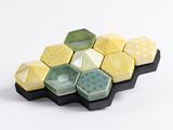 des hexagones en céramique jaunes et verts disposés sur un plateau noir, sur fond blanc