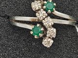 a close up of a diamond and emerald ring on a black surface