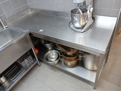 un plan de travail en acier inoxydable équipé d'un mitigeur et sur lequel sont posées des casseroles, dans une cuisine professionnelle