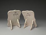 pair of white ceramic chairs with writing on them sitting on a gray surface
