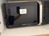 a man taking a picture of a microwave on the shelf