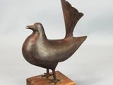 un petit oiseau en bronze posé sur un socle en bois, sur fond blanc