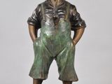 bronze statue of a boy in overalls standing on a black base