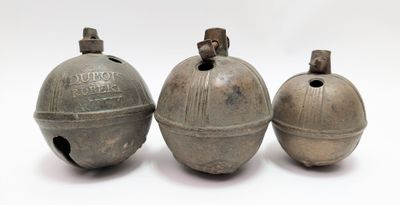 trois vieilles cloches en métal posées les unes à côté des autres sur une surface blanche