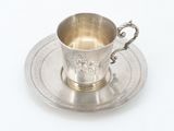 a silver cup and saucer sitting on a saucer