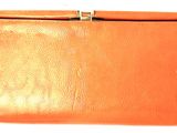 an orange leather purse with a metal clasp on a white background