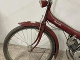 a small red bike parked against a white wall