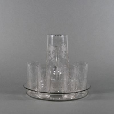 un pichet en verre transparent et des verres posés sur un plateau en argent