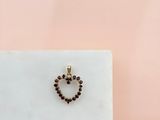 un pendentif en forme de cœur en or, orné de grenats, repose sur un bloc de marbre