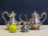 three silver teapots and a green apple on a table