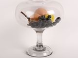 un saladier en verre rempli de fruits et de noix posé sur un plan de travail blanc