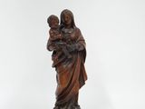 une statue représentant une femme tenant un enfant dans ses bras, posée sur un socle en bois