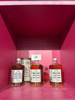 trois bouteilles d'alcool posées sur une étagère, dans une boîte rose