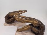 two bronze statues of a woman laying on a marble base