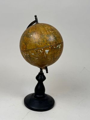 un vieux globe terrestre posé sur un socle noir, avec un fond blanc