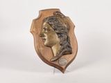 an image of a bronze plaque of a woman ' s head on a wooden stand
