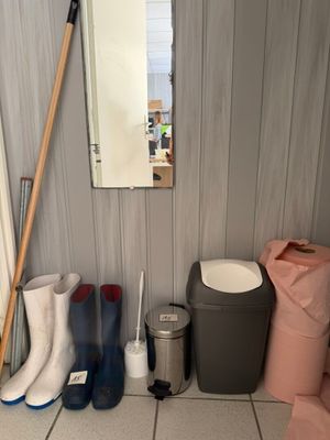 several pairs of rain boots are lined up next to a trash can and a mirror