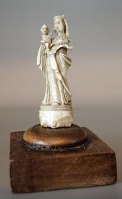 une statue représentant une femme tenant un enfant dans ses bras, posée sur un bloc de bois