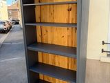 tall grey bookcase with wooden shelves in front of a building