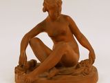 statue d'une femme nue assise sur un socle, les jambes croisées