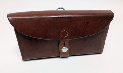 étui en cuir marron pour appareil photo posé sur une surface blanche