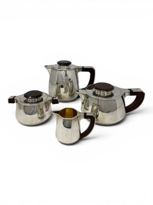 three silver teapots and two cups on a white surface