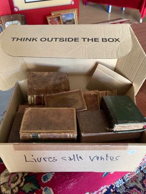 une boîte remplie de livres posée sur une table, avec une pancarte sur laquelle on peut lire « Sortir des sentiers battus »