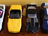 Plusieurs petites voitures sont alignées sur une table devant un mur jaune.