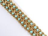 a close up of a gold and turquoise bracelet on a white surface