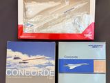 trois livres dans leur boîte posés sur une table, avec un avion en arrière-plan