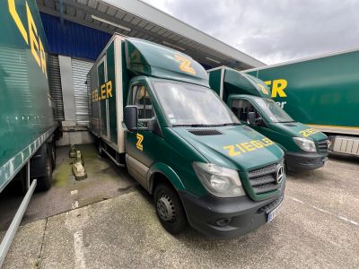 Trois camions de livraison verts sont garés devant un immeuble