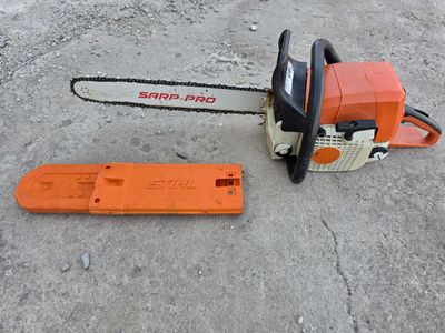 an orange chainsaw sitting on the ground next to a piece of wood