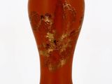 un vase rouge orné de feuilles dorées, posé sur un socle