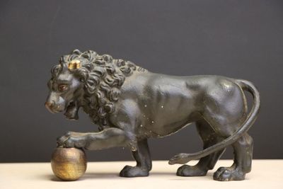 statue of a lion with a ball in its paws on a table