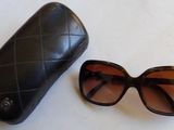 une paire de lunettes de soleil et son étui posés sur une surface blanche, sur fond blanc