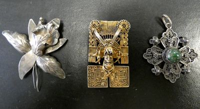 trois pendentifs en argent et en or sur un fond noir orné d'une fleur