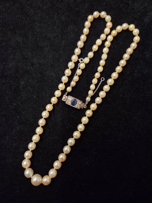 un collier de perles blanches muni d'un fermoir en argent, sur fond noir