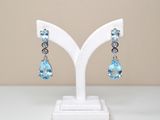 paire de boucles d'oreilles en cristal de topaze bleue et de topaze blanche, présentées sur un socle blanc
