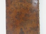 an old brown book sitting on top of a table next to a white wall