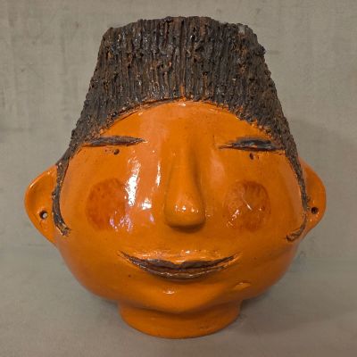 un vase orange orné d'un visage en bois