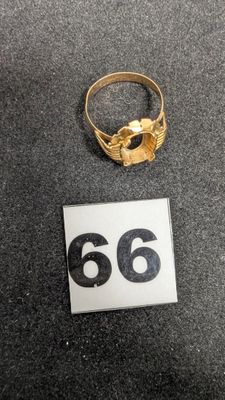 un gros plan d'une bague en or posée sur une table, à côté du chiffre 66