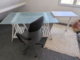 a desk with a glass top and a chair in the corner
