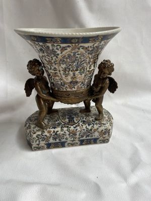 un vase orné de deux chérubins, posé sur un socle