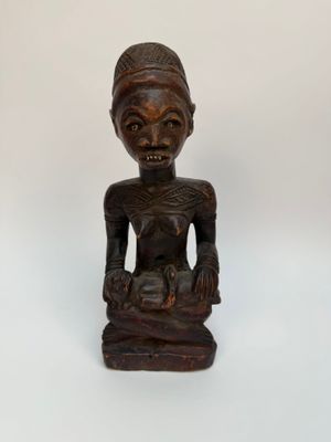 une vieille statue en bois représentant une femme assise sur une surface blanche